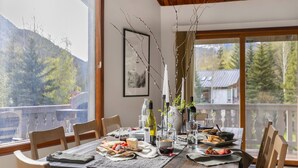 Une table à manger dressée avec des assiettes, des verres et des bouteilles, offrant une vue pittoresque sur des arbres et un bâtiment.