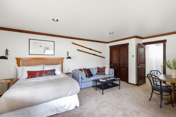 Un dormitorio con cama, sofá, mesa de centro y zona de comedor con sillas.