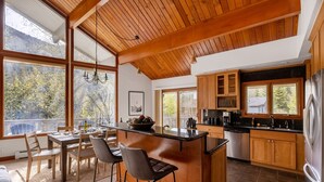 Une cuisine moderne avec des meubles en bois, un îlot central et de grandes fenêtres donnant sur une zone boisée.