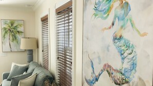 A living room with a grey sofa, a lamp, a small table with a decorative item, and a large abstract painting on the wall.