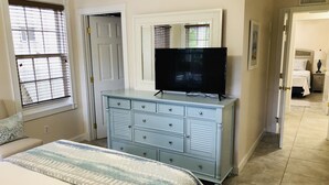 A bedroom with a bed, dresser, television, and a door leading to another room.