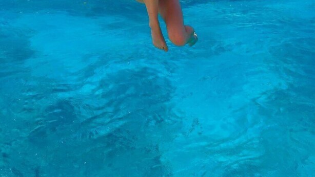 A person in a bikini underwater with a clear blue sky and ocean in the background.