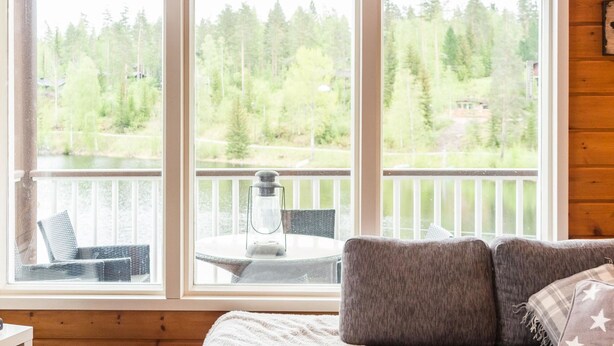 A cabin with a wooden interior, a sofa, a table with a lantern, and a view of a forest through large windows. - Tahkon rantatupa 7 b by Interhome (Nilsiä)