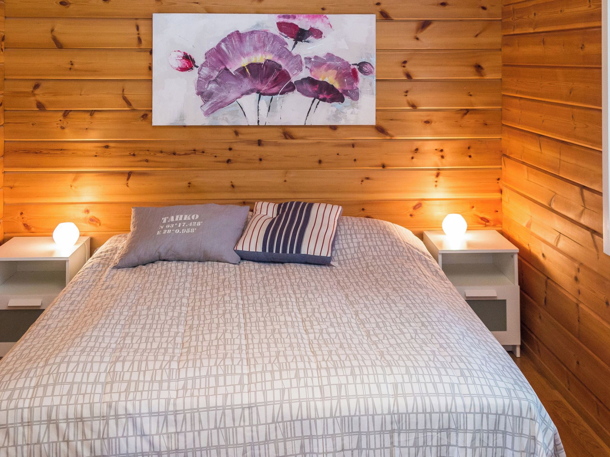 Una habitación con paneles de madera, una cama, dos mesitas de noche y un cuadro de flores.