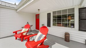 A porch with two red Adirondack chairs, a red door, and a window with shutters.