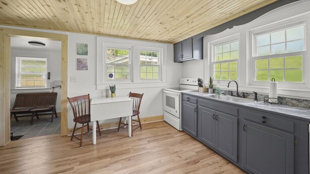 A kitchen with wooden flooring, white cabinets, a built-in oven, and a window overlooking a green landscape.