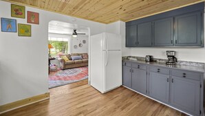 A kitchen with wooden flooring, grey cabinets, a white refrigerator, and a coffee maker on the counter.