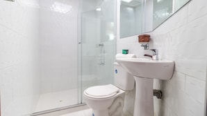 Une salle de bain moderne avec une douche à parois de verre, des toilettes blanches et un lavabo surmonté d’un miroir.