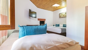 Une chambre avec un plafond en bois, un téléviseur à écran plat, une cheminée, un lit avec un oreiller bleu et une fenêtre donnant sur un beau paysage.