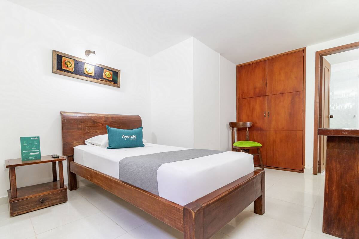 A neatly arranged hotel room with a wooden bed, a bedside table, a green chair, and a wardrobe.