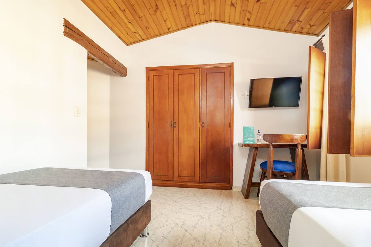 A room with two beds, a wooden wardrobe, a desk with a chair, and a television on the wall.