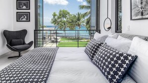 Una camera da letto con un letto grande, una sedia e un balcone che si affaccia sull'oceano e su palme.