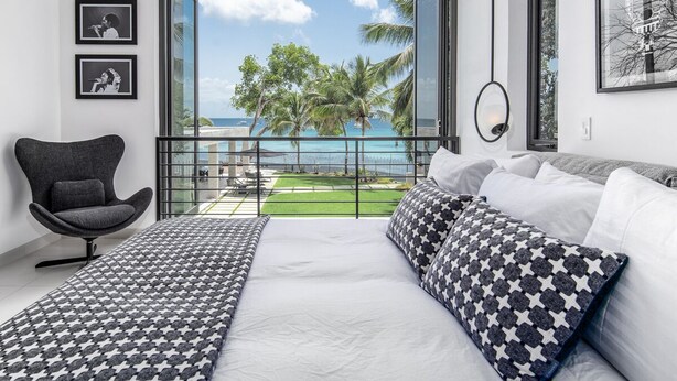 Une chambre dotée d’un grand lit, d’une chaise et d’un balcon offrant une vue sur l’océan et les palmiers.