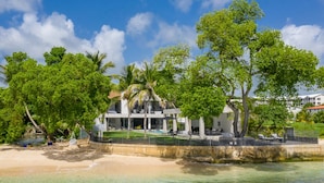 Une propriété située en bord de mer, avec une grande maison, des palmiers et une vue dégagée sur l’océan.