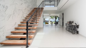 Un intérieur moderne avec un escalier en bois, un plafond haut et une vue sur l’extérieur.