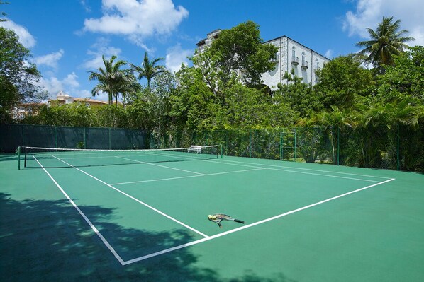 A tennis court with a net, surrounded by trees and a building in the background. - Glamorous Beachfront Estate - Leamington (Battaleys)
