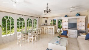 A spacious living area with a dining table, white chairs, a glass coffee table, and a bookshelf. - Glamorous Beachfront Estate - Leamington (Battaleys)