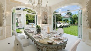 Un comedor ornamentado con una mesa de vidrio dispuesta para una comida, rodeado de sillas blancas.