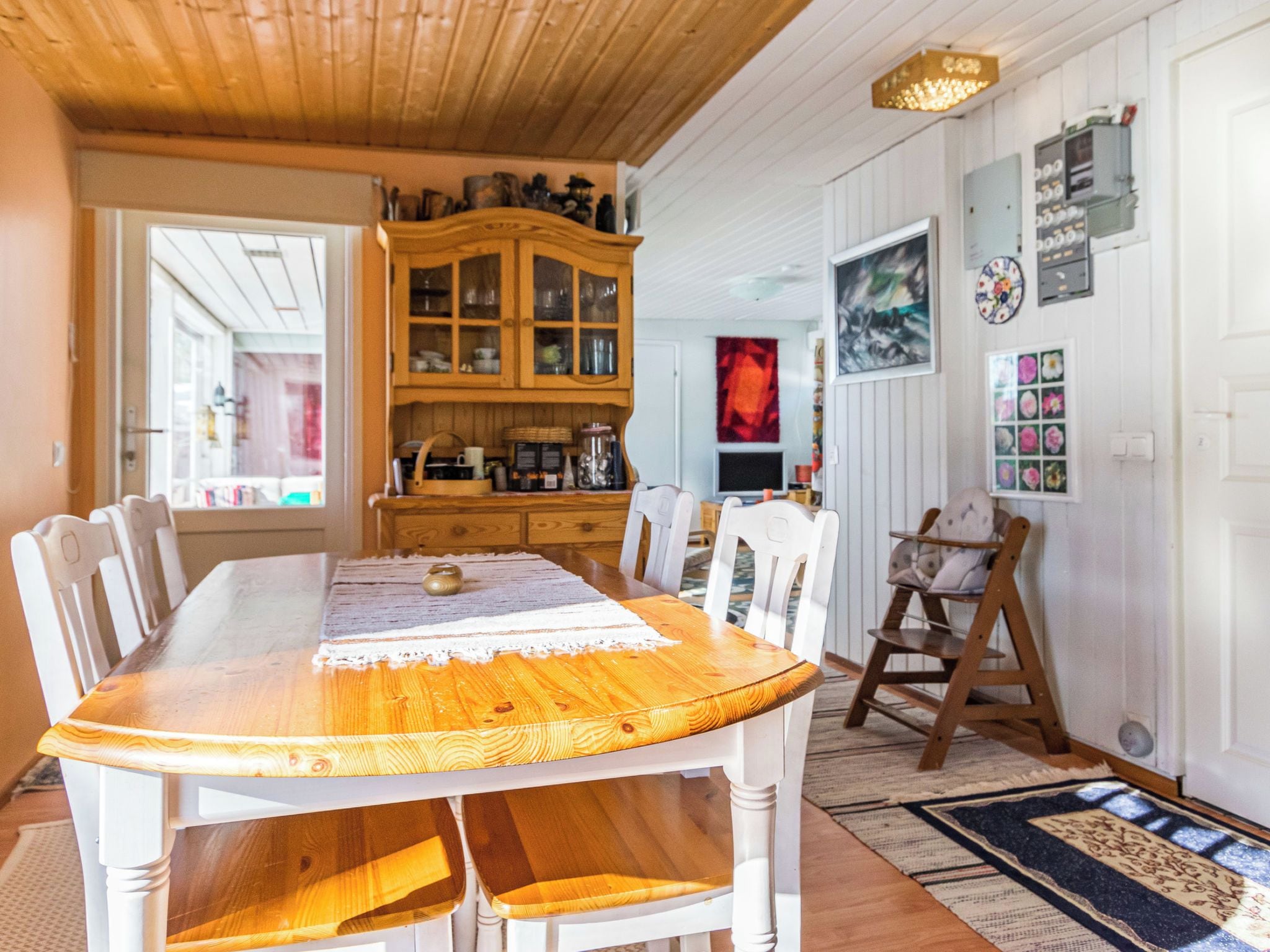 A dining area with a wooden table, white chairs, a wooden cabinet with glass doors, and a red abstract painting on the wall.