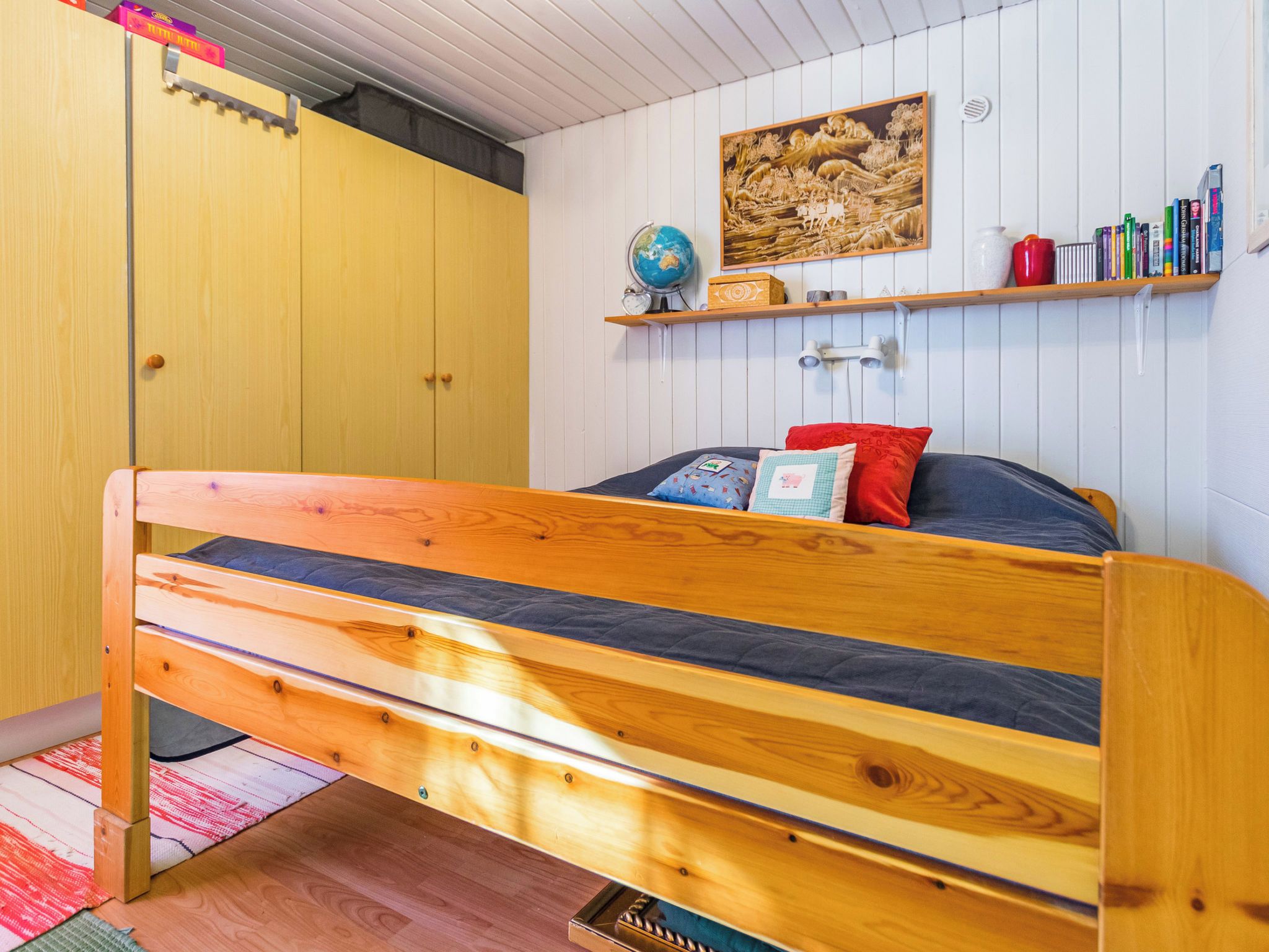 A bedroom with a wooden bed, a globe, a shelf with books, and a painting on the wall.