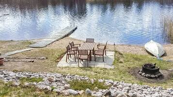 Un espace extérieur aménagé au bord du lac, avec une table et des chaises, un quai et un foyer.