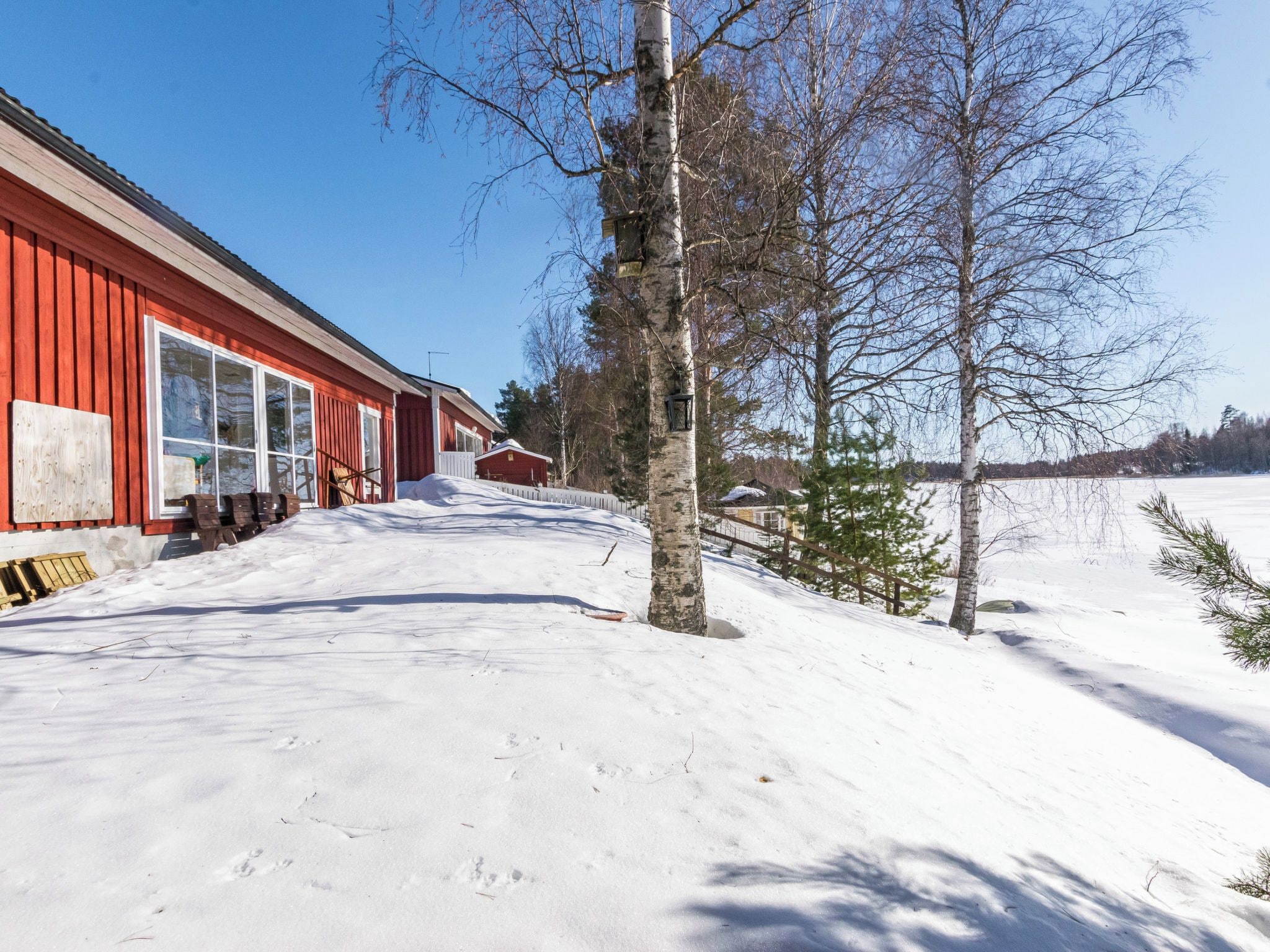 A snow-covered landscape with a red building, a wooden fence, and leafless trees.