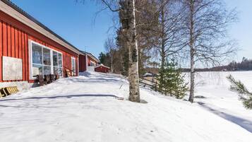 A snow-covered landscape with a red building, a wooden fence, and leafless trees.