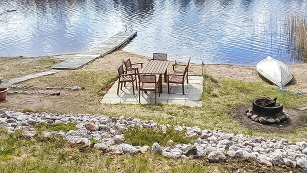 En picnicplads ved søen med bord og stole, en båd og en grill.