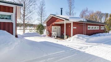 A red wooden building with a covered porch and a door, surrounded by snow.
