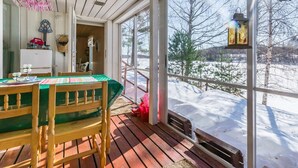 En træterrasse med et bord og stole, store vinduer med udsigt over et sneklædt landskab.