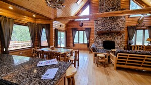 A log cabin interior with a stone fireplace, wooden furniture, and large windows. - Luxury Family Cabin in a forest with a private pond (Necedah)