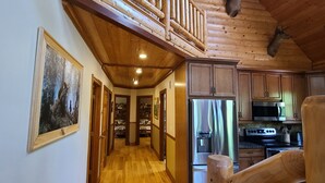 A spacious wooden interior with a high ceiling, a staircase leading to an upper level, and a kitchen area with modern appliances. - Luxury Family Cabin in a forest with a private pond (Necedah)