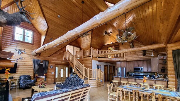 A spacious log cabin with a high ceiling, a staircase, a dining area with a wooden table and chairs, and a kitchen area. - Luxury Family Cabin in a forest with a private pond (Necedah)