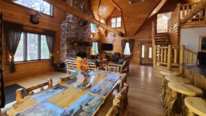 A rustic cabin interior with a stone fireplace, wooden dining table with antlers, and a staircase. - Luxury Family Cabin in a forest with a private pond (Necedah)