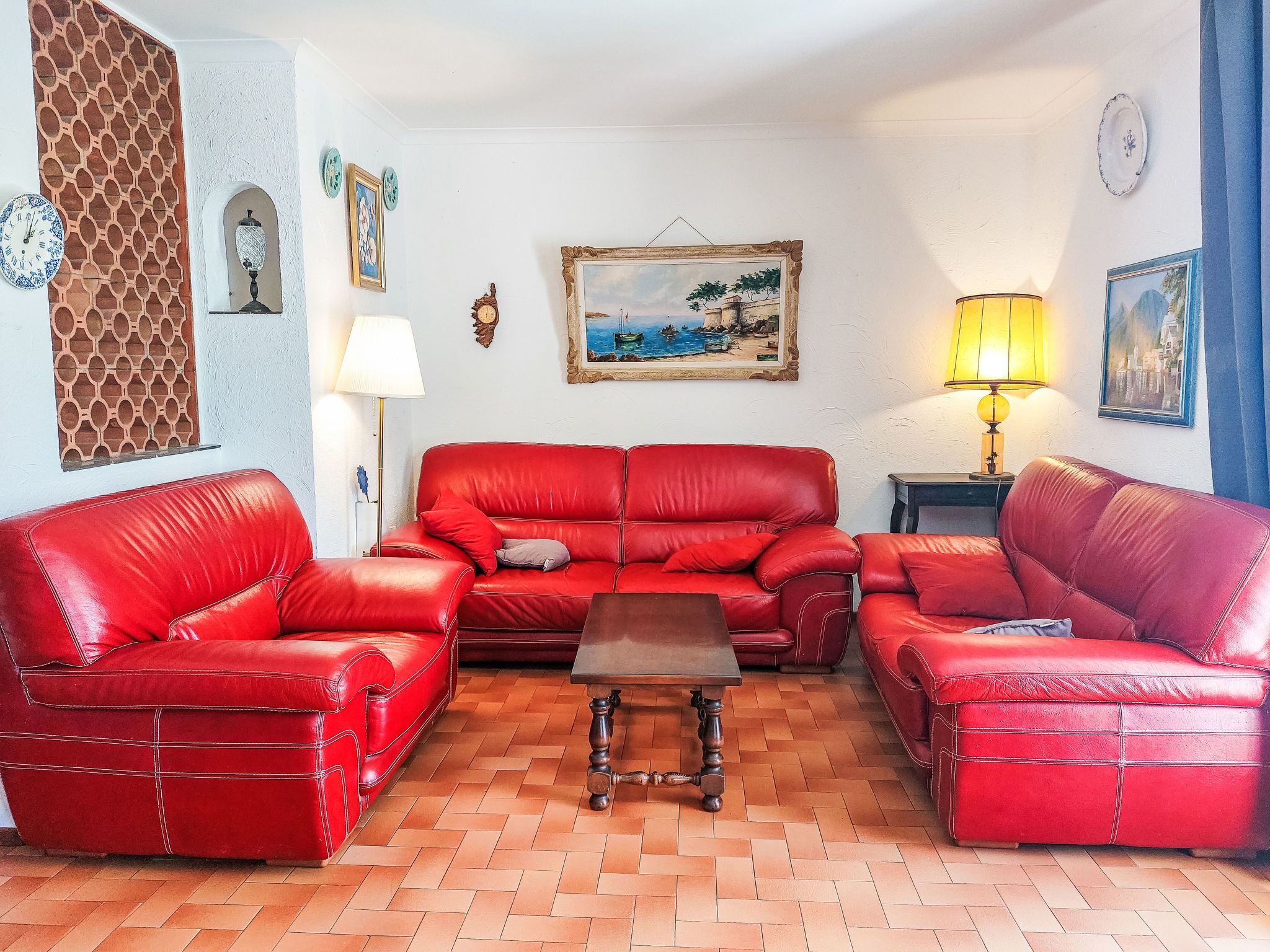 Una sala de estar con un sofá de cuero rojo, una mesa de centro de madera y piso de baldosas.
