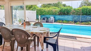Een terras met buitenmeubilair en zwembadzicht, met een tafel gedekt voor vier personen, stoelen en uitzicht op het zwembad en groen.