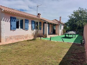 Uma casa com telhado de cerâmica, alicerce de pedra e um pequeno jardim com uma mesa e cadeiras.