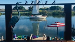 Een houten terras met een zeilboot op het water, kano's en een rood-witte parasol.