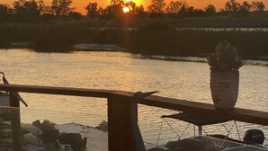 Zonsondergang vanaf een balkon met een vuurplaats, een bloempot en een boot in de verte.