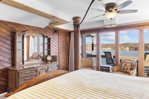A bedroom with a large bed, wooden walls, a dresser, a chair, and a view of a lake. - Viewhouse 24 - Five Bedroom House, Sleeps 12 (Sunrise Beach)