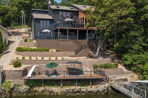 Ein zweistöckiges Haus mit einer Terrasse, Sitzgelegenheiten im Freien und einem kleinen Wasserfall.