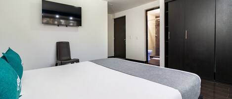 A hotel room with a bed, a chair, a TV mounted on the wall, and a wardrobe.