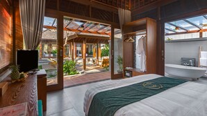 A modern hotel room with a large bed, a TV, a desk with a computer, and a bathroom with a bathtub. - Alam Wayang Ubud (Ubud)