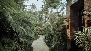 A narrow pathway flanked by dense tropical foliage leading to a brick building with a sign. - Alam Wayang Ubud (Ubud)
