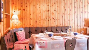 Un acogedor comedor de madera con una mesa preparada para cuatro personas, bancos con cojines de cuadros y una lámpara fijada a la pared.