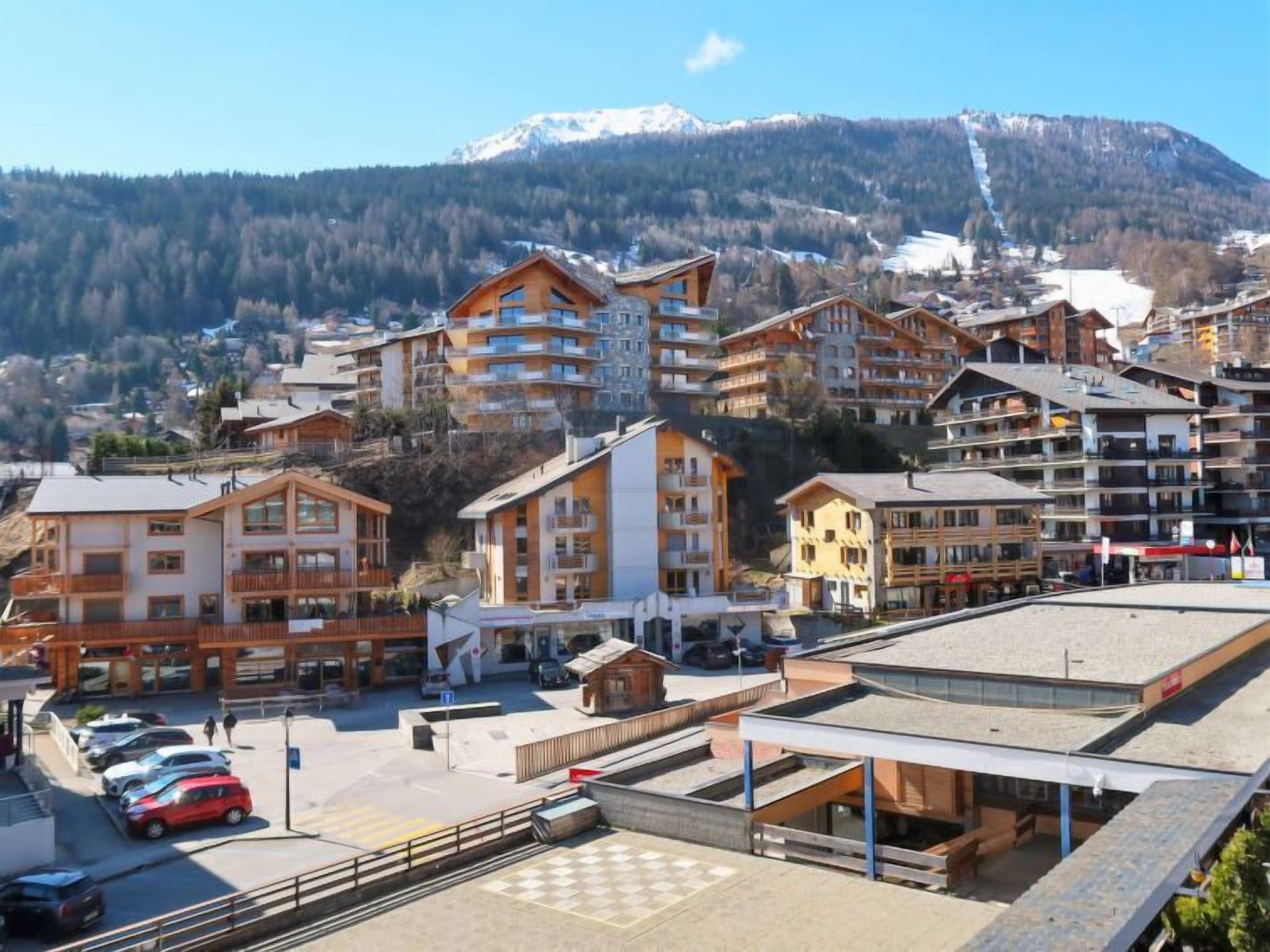 Ein Bergresort mit mehrstöckigen Gebäuden, einem Parkplatz und Blick auf schneebedeckte Berge.