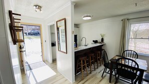 A modern kitchen with a bar area, wooden stools, and a dining table with chairs. - Oz Festival! Walk to Resort! Pets! Fireplace! (Beech Mountain)