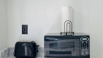 A microwave oven on a wooden stand with a paper towel holder on top, a toaster, and a power outlet on the wall.