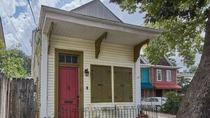 Une maison à deux étages avec une porte rouge, des volets verts et un petit porche doté d’une balustrade noire.