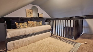 Une chambre mansardée chaleureuse avec un plafond en pente, un lit en bois foncé avec une literie blanche, un tapis blanc moelleux et un panneau mural à rayures.